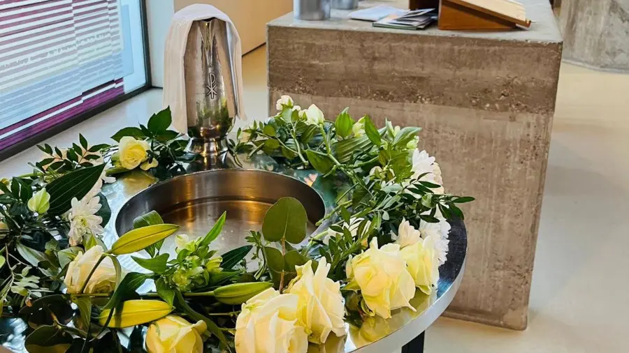 Das Taufbecken ist mit weißen Rosen und Efeu geschmückt.