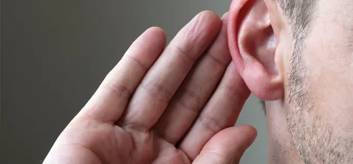 Nahaufnahme eines menschlichen Ohrs. Eine Hand ist seitlich an das Ohr gelegt, als wolle die Person besser zuhören oder etwas genauer wahrnehmen.