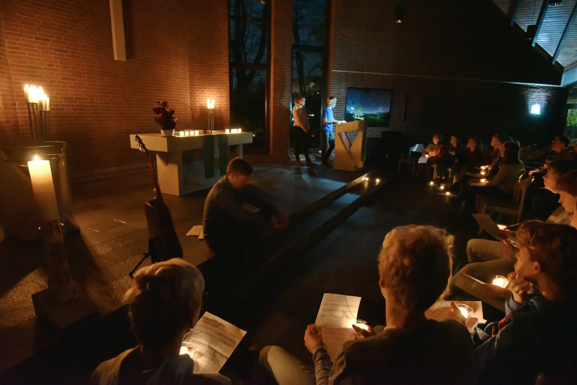 Das Foto zeigt eine Gruppe von Menschen beim Gottesdienst. Die Kirche ist abgedunkelt, die Anwesenden halten Kerzen in ihren Händen.