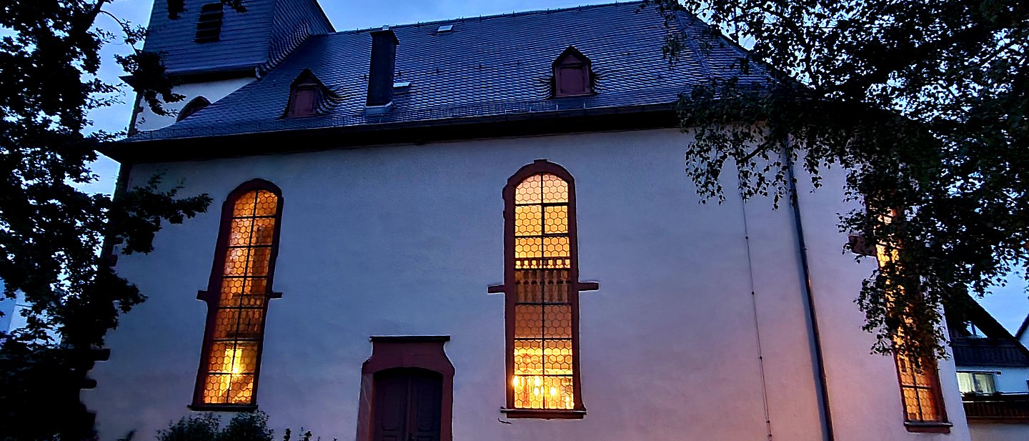 Außenansicht der Kirche im Abendlicht mit beleuchteten Kirchenfenstern