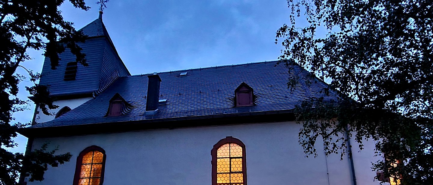 Außenansicht der Kirche im Abendlicht mit beleuchteten Kirchenfenstern