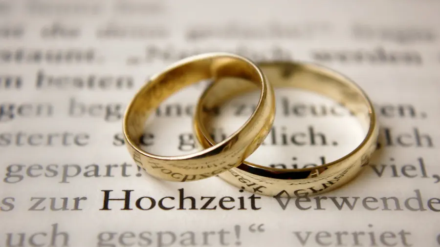 Zwei Trauringe liegen halb übereinander auf einem Text, in dem das Wort Hochzeit hervorgehoben ist.
