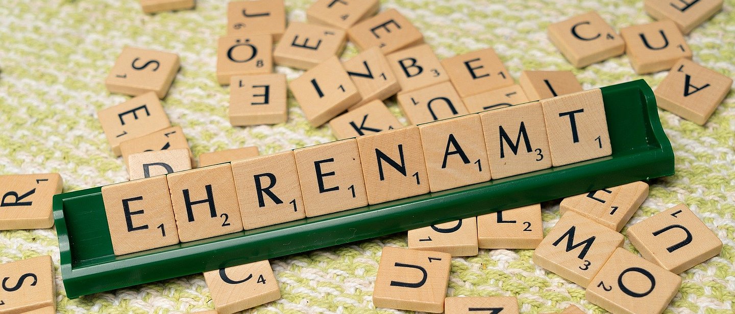 Es wird ein Scrabblespiel gezeigt mit vielen Steinen. Auf der Bank steht das Wort Ehrenamt. 