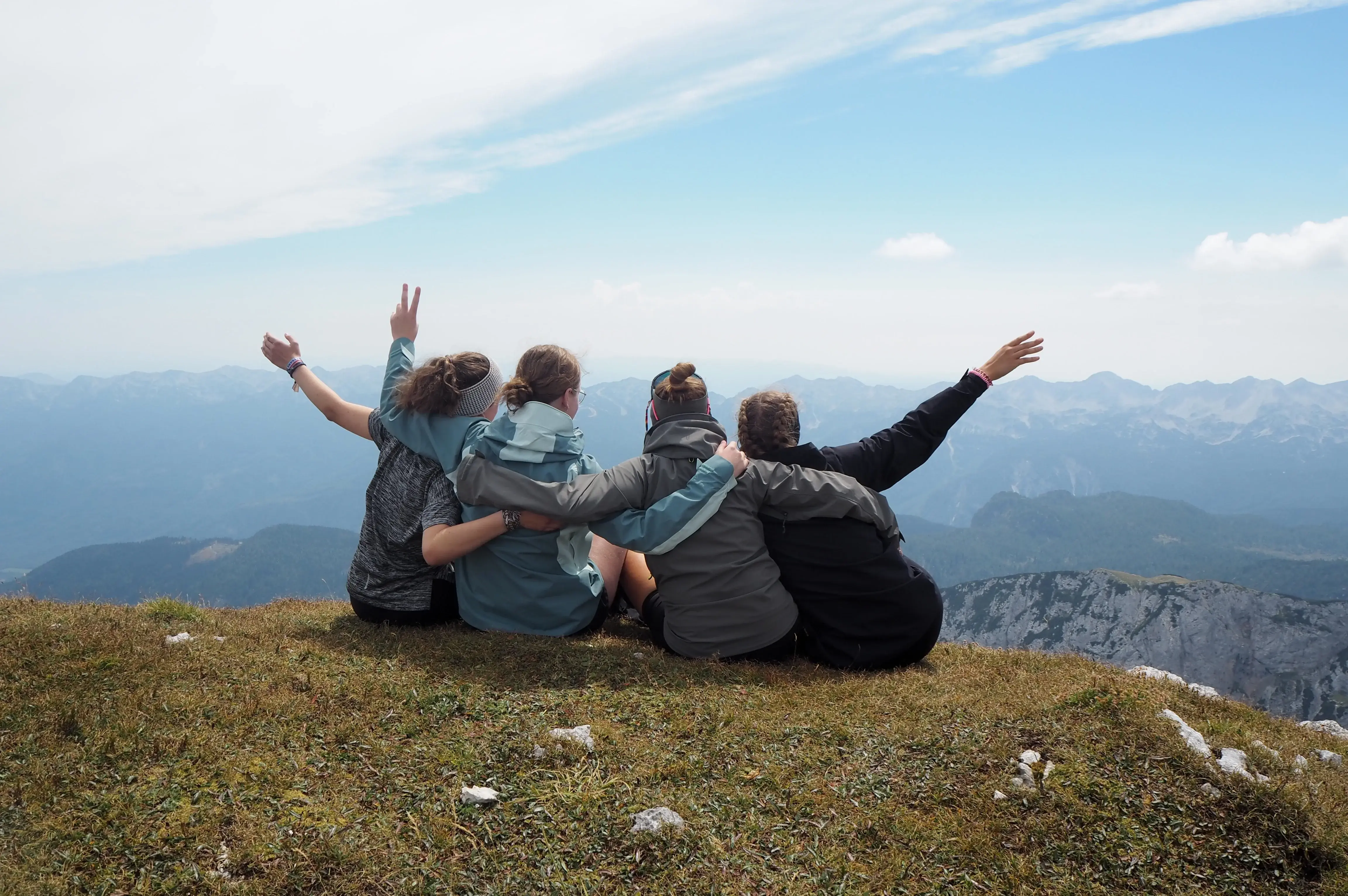 Bei einer Jugendfreizeit in Slowenien sitzen vier Jugendliche mit dem Rücken zur Kamera auf einem Berg und schauen in das Tal.