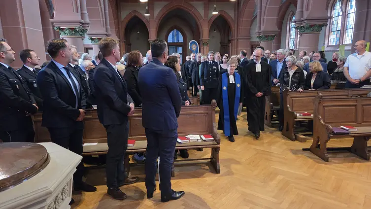 Durch den Mittelgang der Kirche kommen die Mitwirkenden, die Besucherinnen stehen und schauen auf die Hereinkommenden.