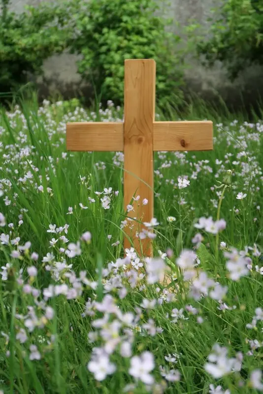 Kreuz Nahaufnahme von einem Holzkreuz aus kleinen schlichten Balken. Das Kreuz steht in einer Frühjahrswiese in sattem Grün mit zarten weißen Blümchen.