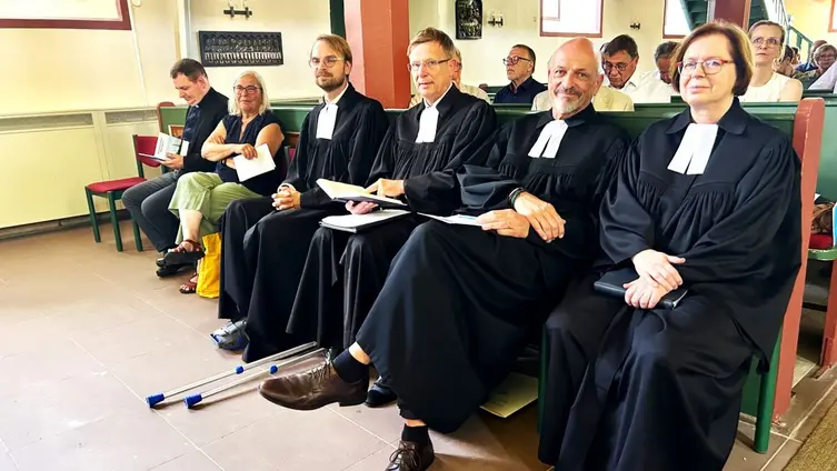 Vier Pfarrer*innen mit Talaren sitzen in der ersten Kirchenbank