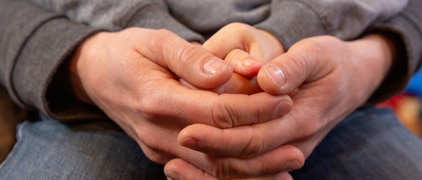 Junge und Erwachsener halten ihre zum Gebet verschränkten Hände ineinander.
