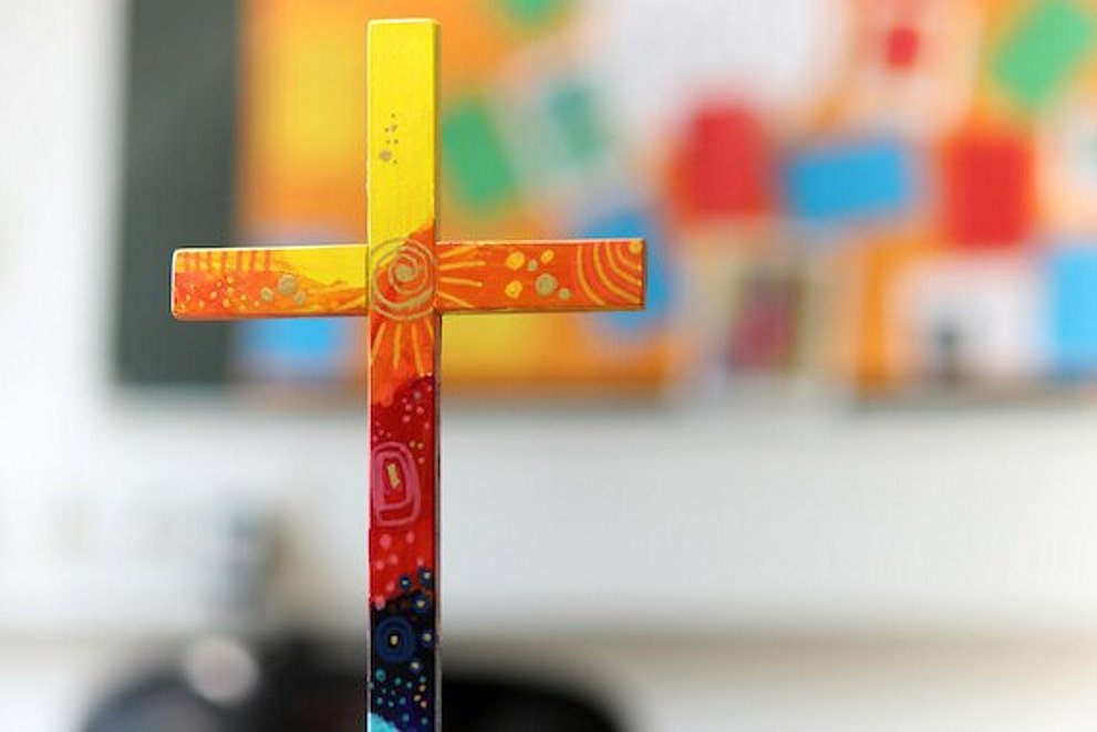 buntes Holzkreuz auf Tuch auf einem Tisch.