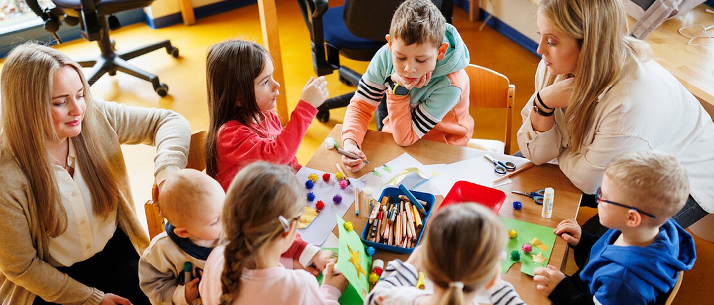 Kinder und Erzieherinnen einer Kita-Gruppe spielen am Tisch.