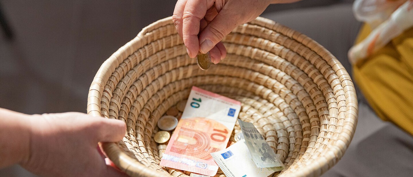 Ein geflochtenes Körbchen wird herumgereicht, um Geld einzusammeln. Ein paar Scheine und Münzen befinden sich bereits darin.