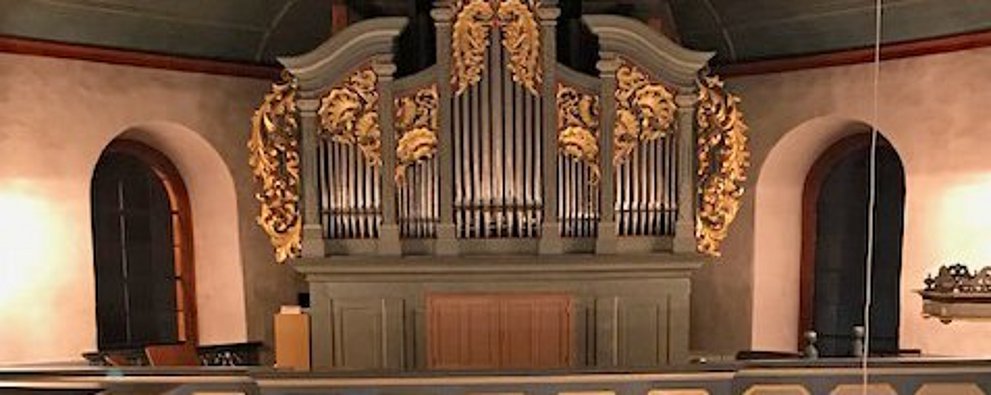 Blick während eines Konzertes in der evangelischen Kirche Köppern von der Rückempore über dem Haupteingang auf den Altarraum und Empore mit Orgel darüber. Vor dem Alter sitzt der Künstler mit Akkordeon.