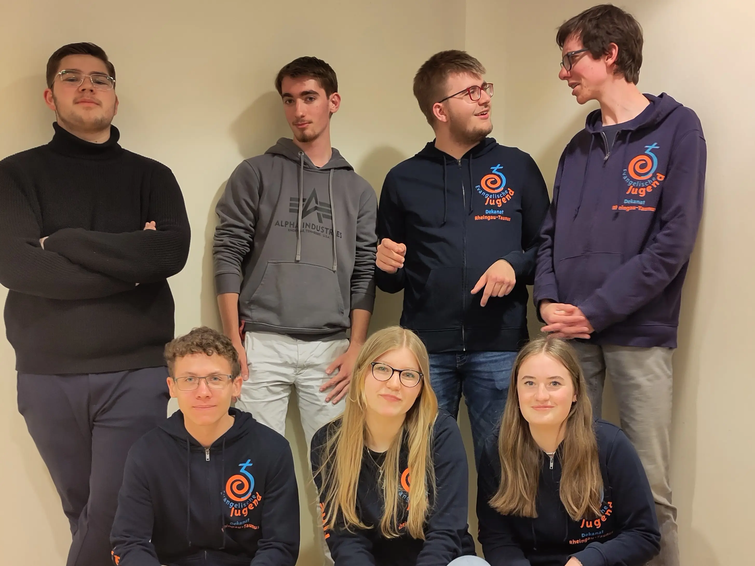 Die Evangelische Jugendvertretung 2024: Sieben Jugendliche posieren in blauen Sweatjacken mit EJHN Logo in einer Raumecke.