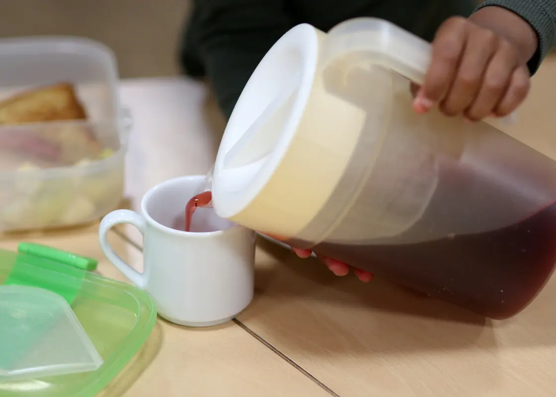 Kind schenkt sich Tee aus einer Kanne in eine Tasse ein