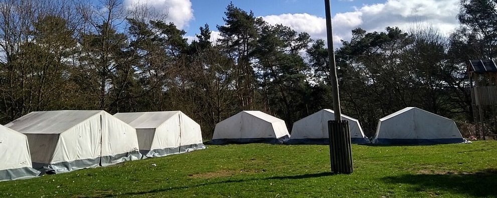weiße große Zelte auf einer Wiese, großes Kreuz in der Mitte, blauer Himmel