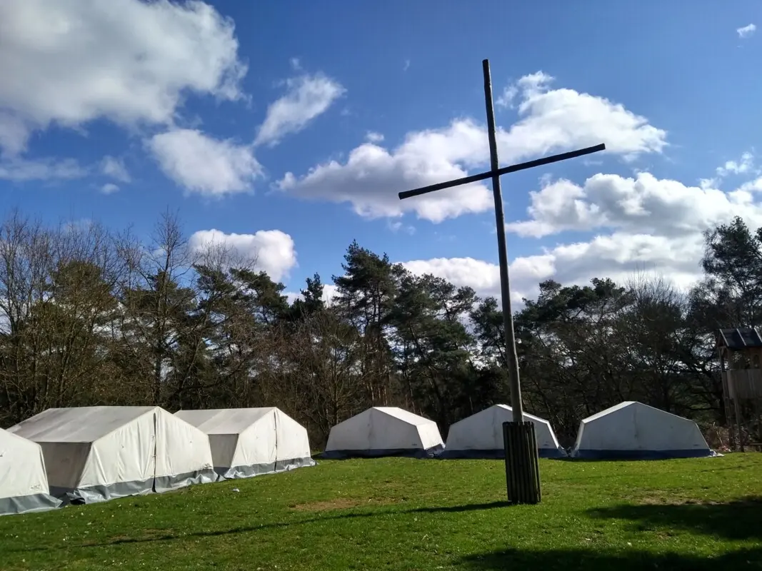 weiße große Zelte auf einer Wiese, großes Kreuz in der Mitte, blauer Himmel