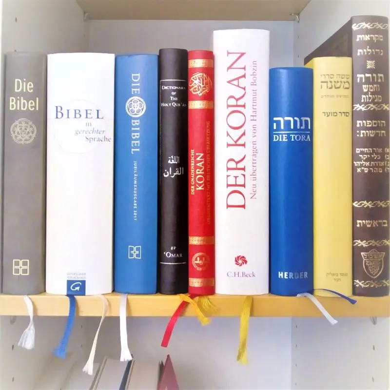 Interreligiöser Dialog In einen Bücherregal stehen nebeneinander je drei verschiedene Ausgaben der Bibel, des Korans sowie zwei Ausgaben der Tora und eine Mischna