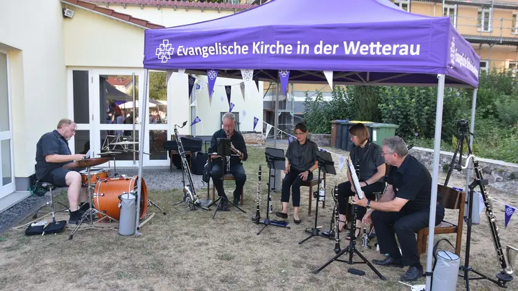 Fünf Musikerinnen und Musiker, vier Klarinetten und ein Schlagzeug, alle in schwarzer Kleidung, unter einem lila Pavillon mit dem Aufdruck Evangelische Kirche in der Wetterau.