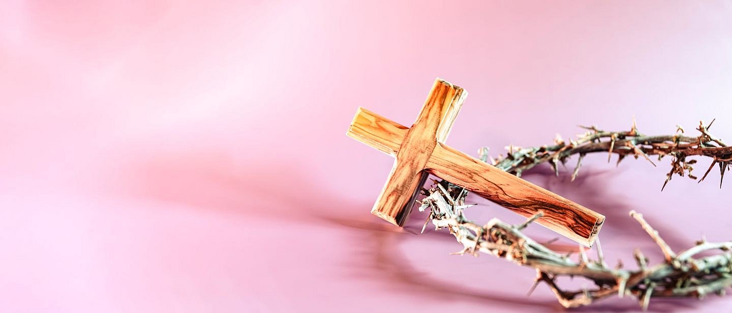 Ein Holzkreuz liegt auf einem Dornenkranz auf einem rosa Untergrund