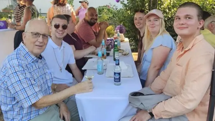 Gruppe von Menschen an einem Tisch, alle haben Getränke vor sich und schauen in Richtung Kamera.