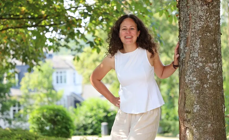 Gemeindepädagogin Nadine Bongard lehnt an einen Baumstamm vor grünen Blättern