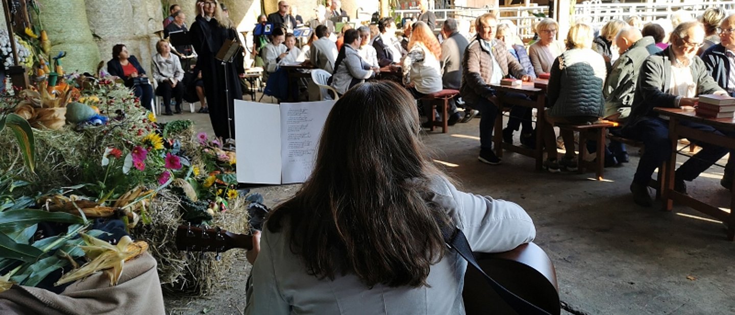 Gottesdienst in Neunkirchen im Vordergrund eine Gitarristin im Hintergrund die Gemeinde mit Pfarrerin unter einer Pergola.