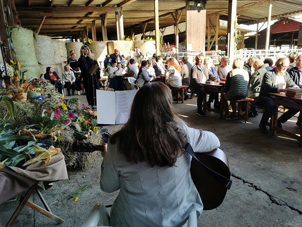 Gottesdienst in Neunkirchen im Vordergrund eine Gitarristin im Hintergrund die Gemeinde mit Pfarrerin unter einer Pergola.