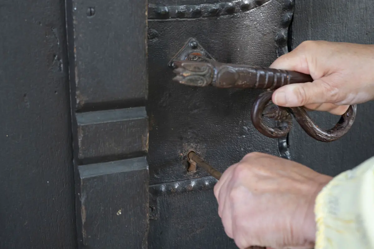 Nahansicht, wie eine rechte Hand eine Klinke drückt, während die linke Hand einen Schlüssel in das Schlüsselloch schiebt.