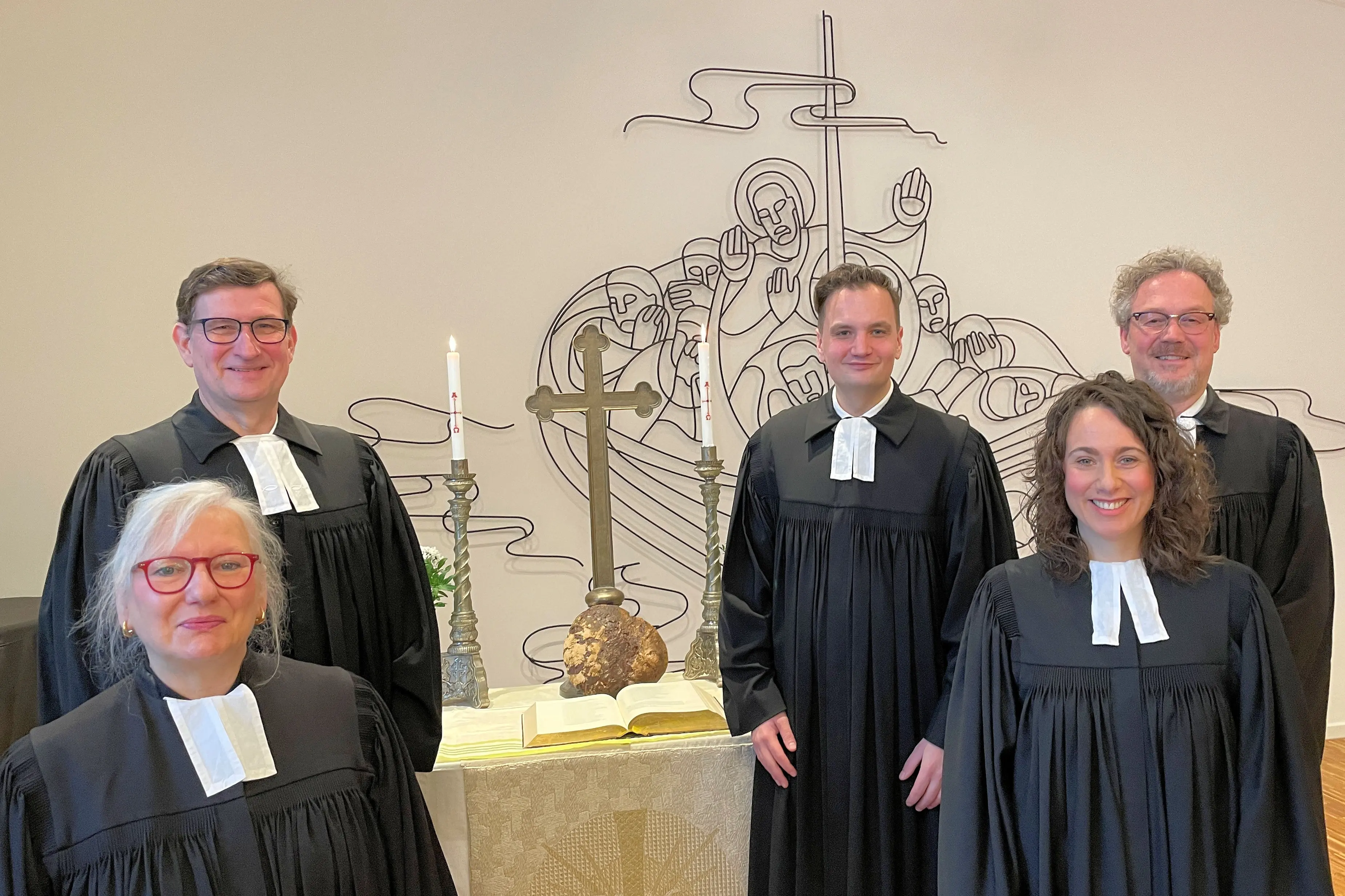 Zwei Pfarrerin und drei Pfarrer im Talar vor einem Altar