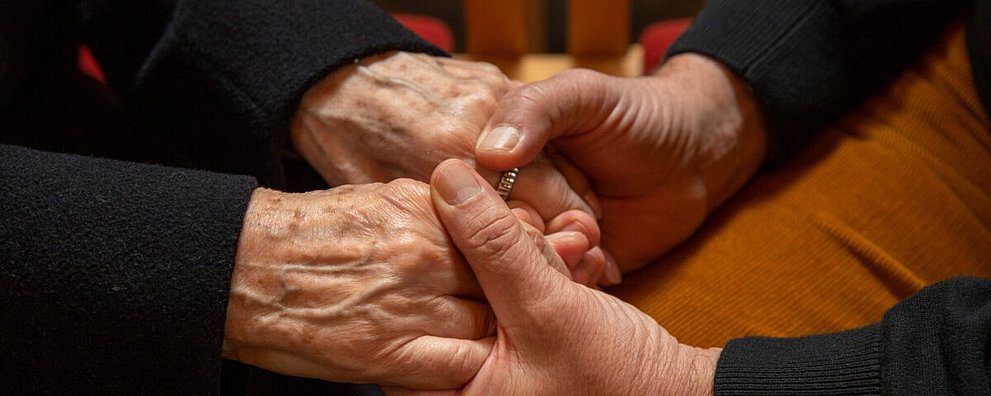 Zwei Menschen halten einander die Hände im gemeinschaftlichen Gebet.
