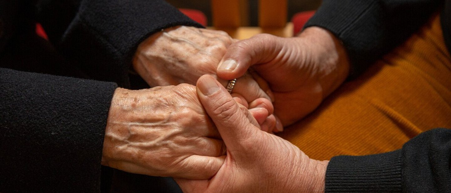 Zwei Menschen halten einander die Hände im gemeinschaftlichen Gebet.