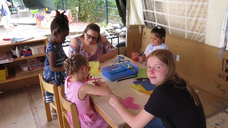 Kinder sitzen mit Erzieherinnen am Kindertisch