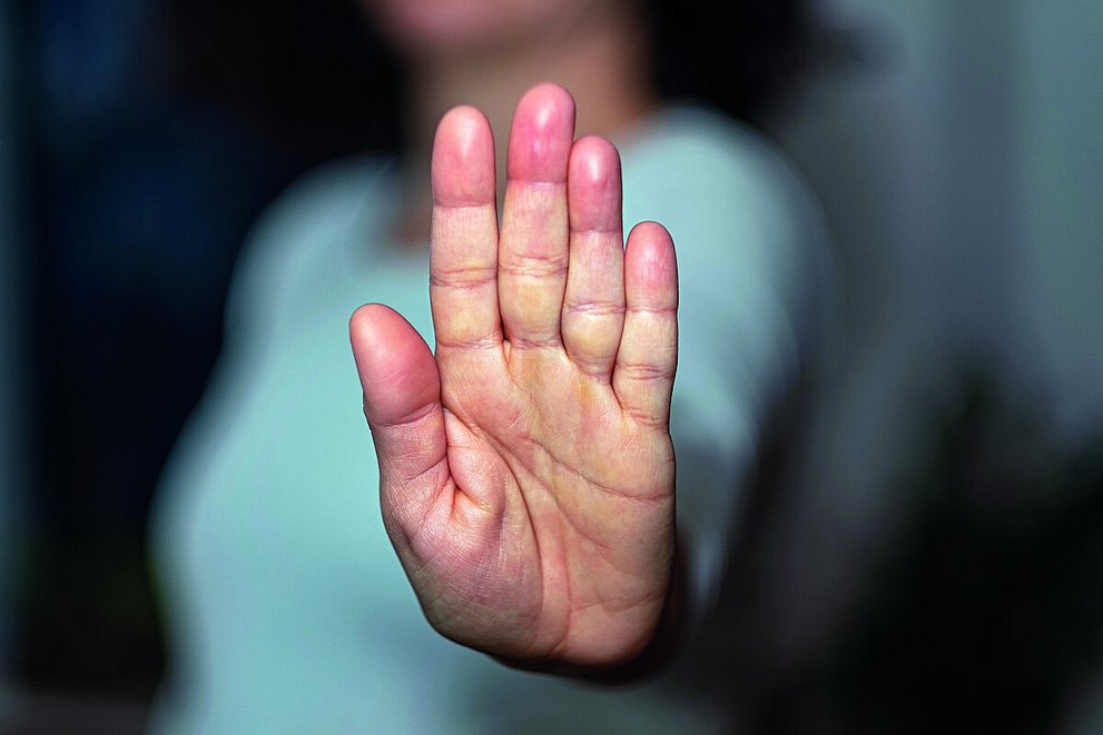 Eine Frau streckt ihre Handfläche aus und in die Kamera. Der Fokus liegt auf der Handfläche, der Rest ist verschwommen.
