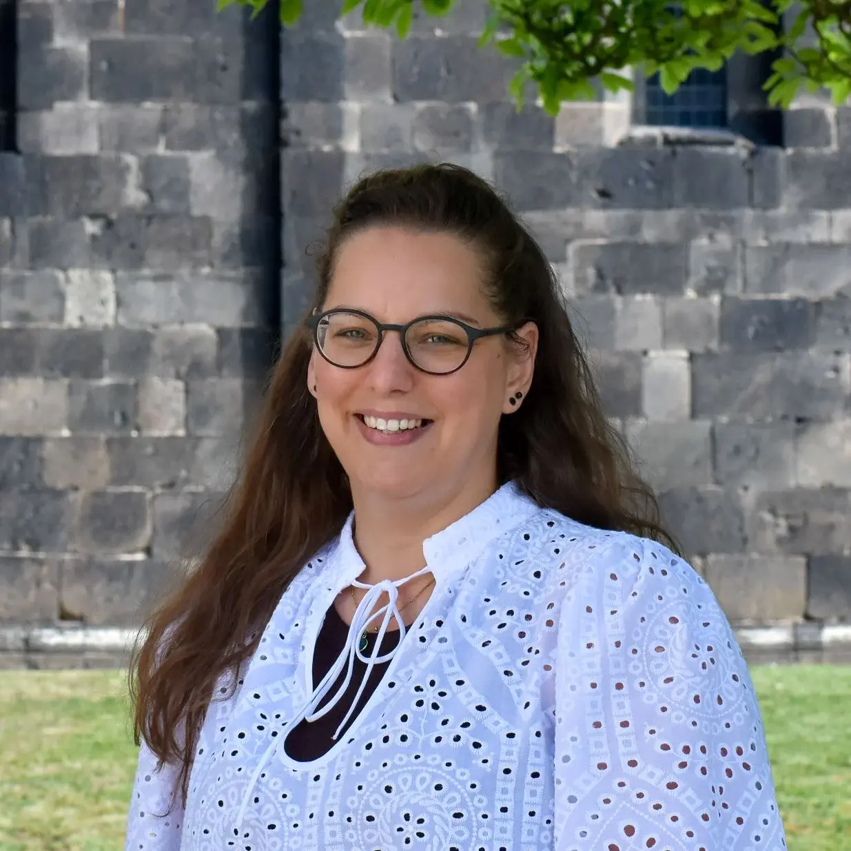 Porträt einer jungen Frau mit Brille, im Hintergrund eine Kirche und grüne Wiese.