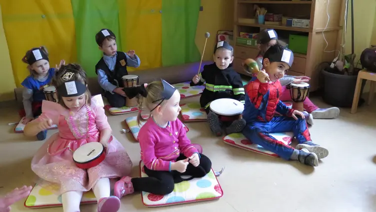 Kinder sitzen am Boden und machen mit Tromelen Musik