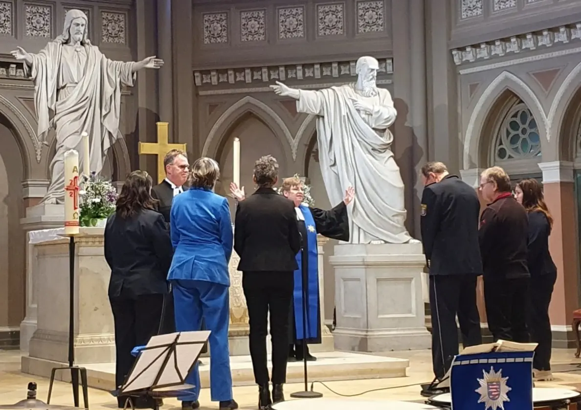 Die Pfarrerin spendet den Segen für einige Personen, die im Altarraum stehen. Im Hintergrund große Steinfiguren, die Jesus Christus und einen Apostel zeigen.