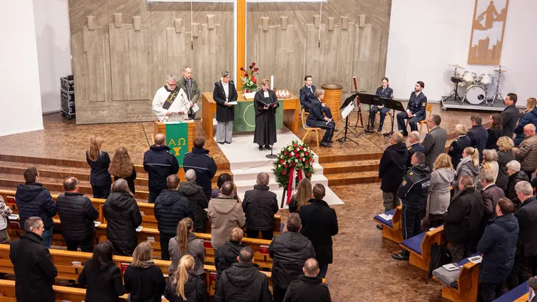 Im Inneren der Paul-Gerhardt-Kirche stehen die Besucher in den Reihen. Im Altarraum stehen die Pfarrerin, der Diakon und weitere Beteiligte. Das kleine Orchester sitzt rechts.