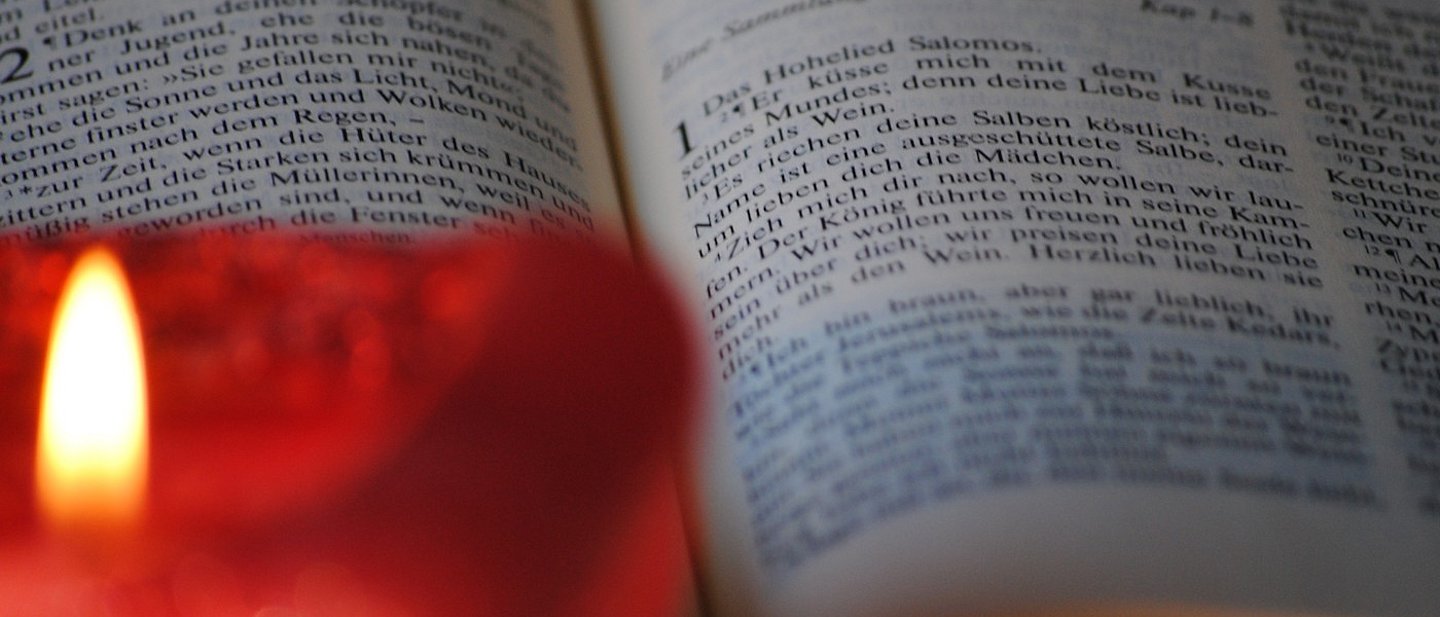 Rote brennende Kerze im Vordergrund, dahinter aufgeschlagene Bibel mit dem Hohelied Salomos.