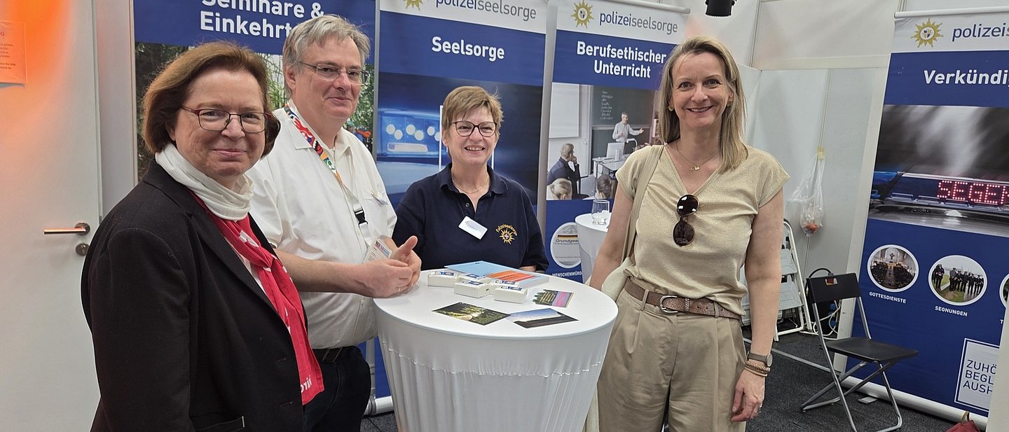 Die vier Personen stehen an einem Stehtisch am Stand der Polizeiseelsorge.