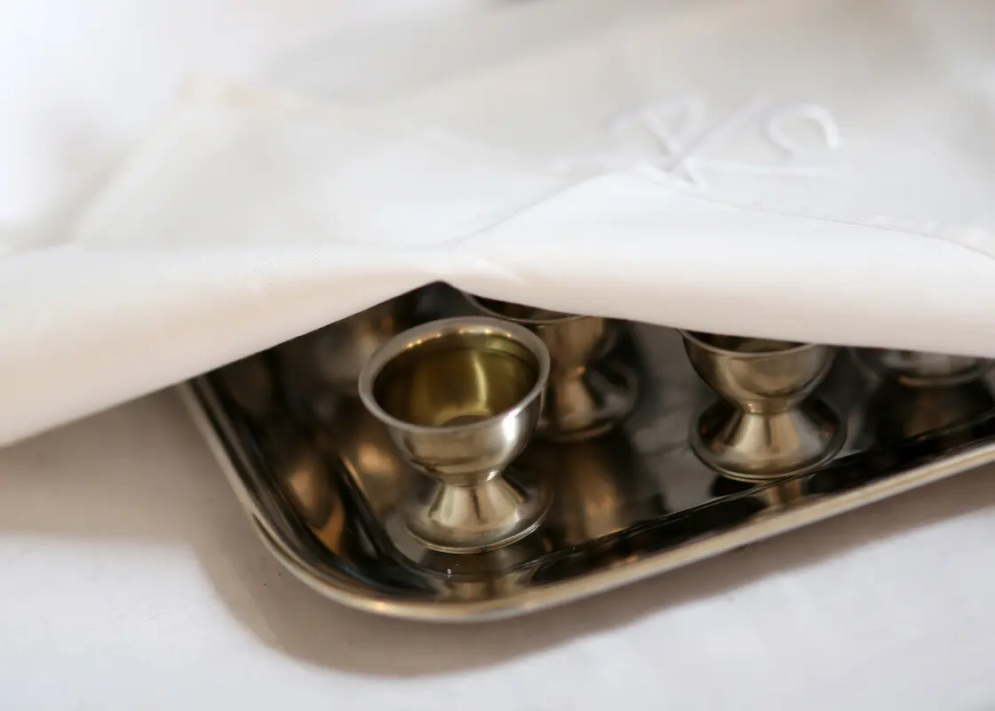 Das Tuch ist leicht gelüftet, man sieht einen Kelch.