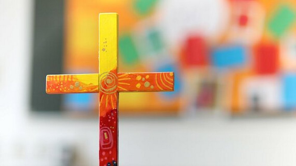 buntes Holzkreuz auf Tuch auf einem Tisch.