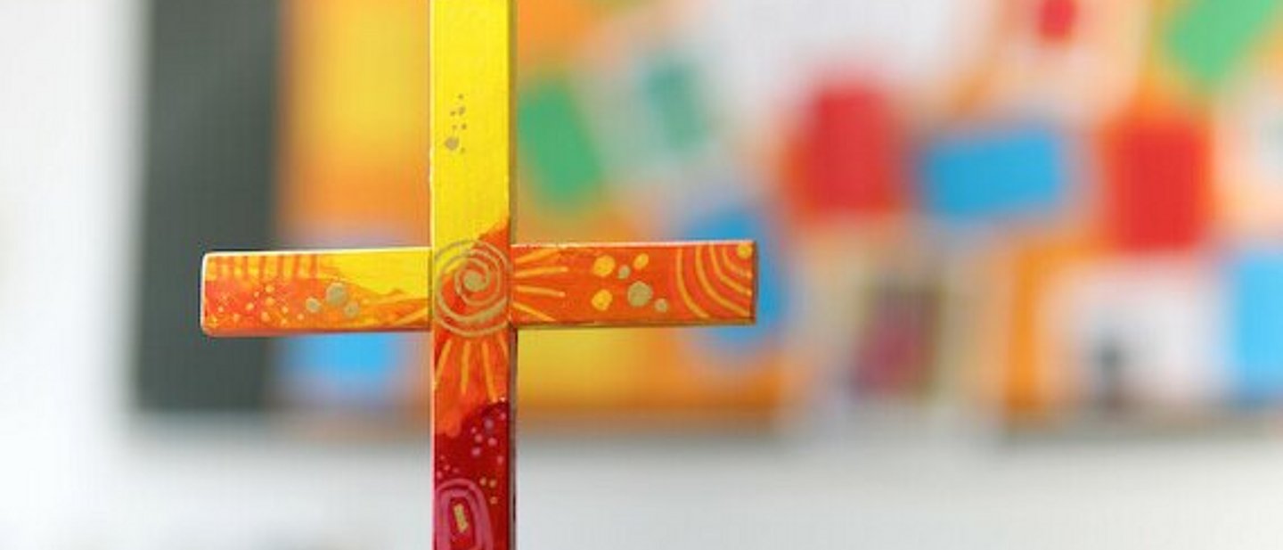 buntes Holzkreuz auf Tuch auf einem Tisch.