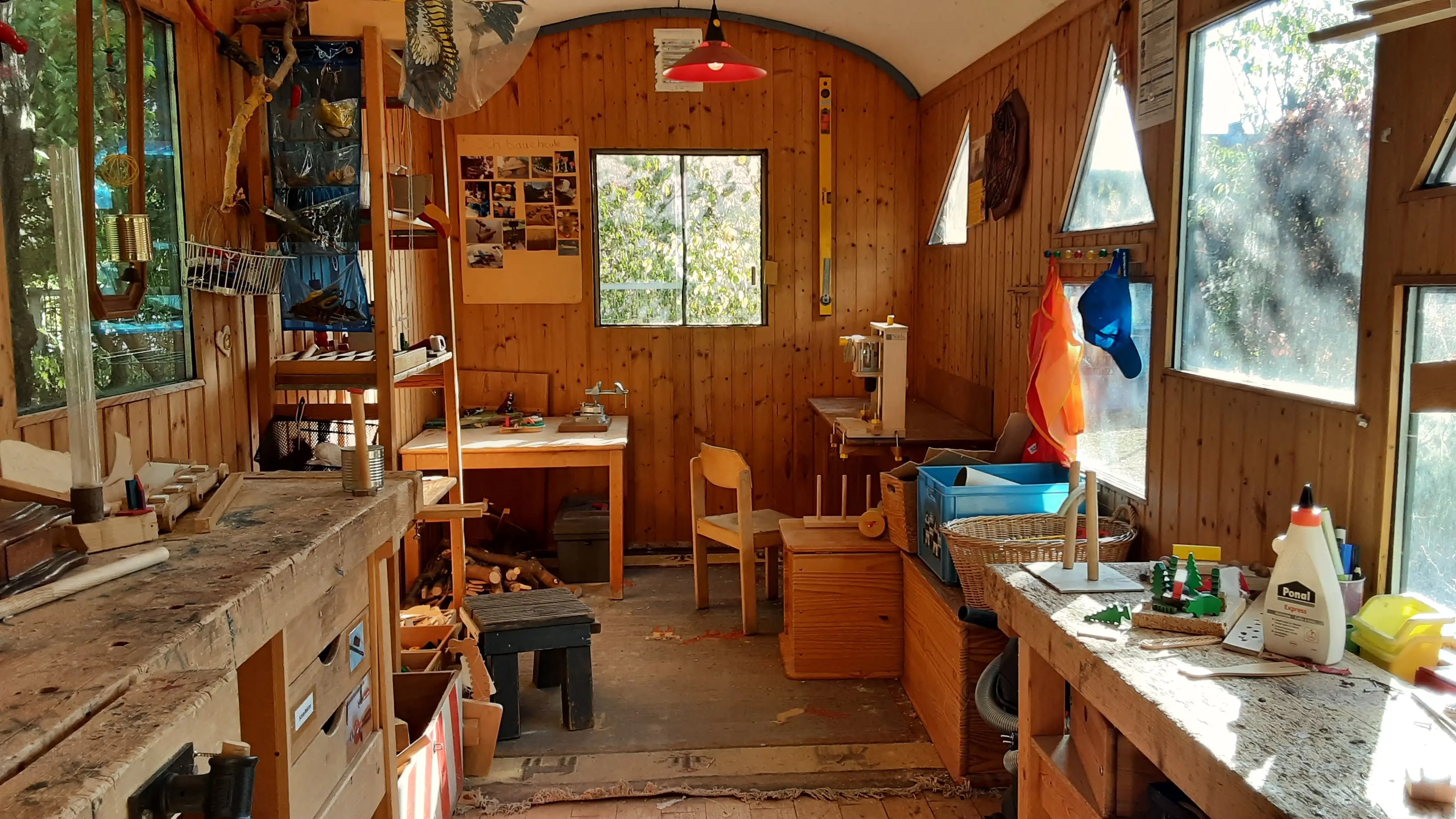 Unsere Holz-Werkstatt im Bauwagen. Mit Werkbänken an beiden Seiten des Bildes und einem Regal. Im Hintergrund ein Fenster in den Garten.