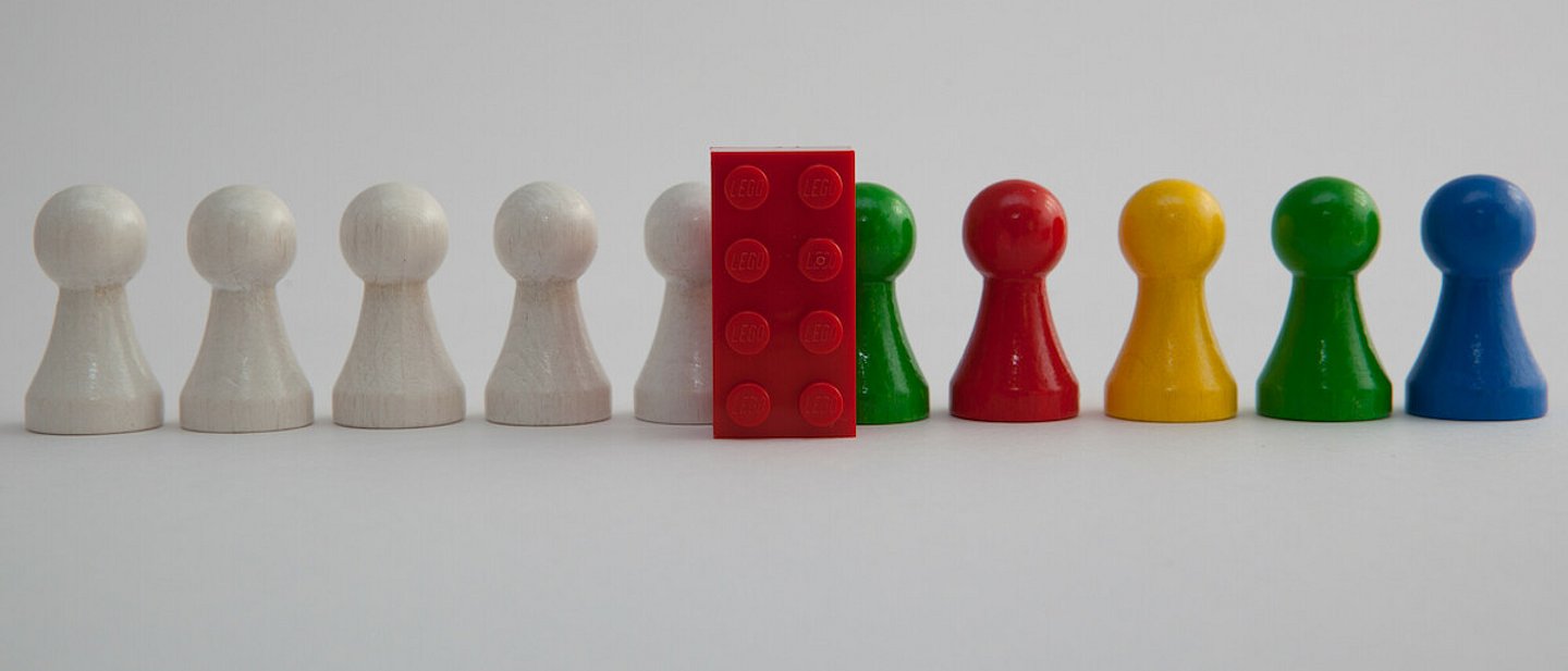 Weiße Spielfiguren laufen hinter einem LEGO Stein durch und werden bunt