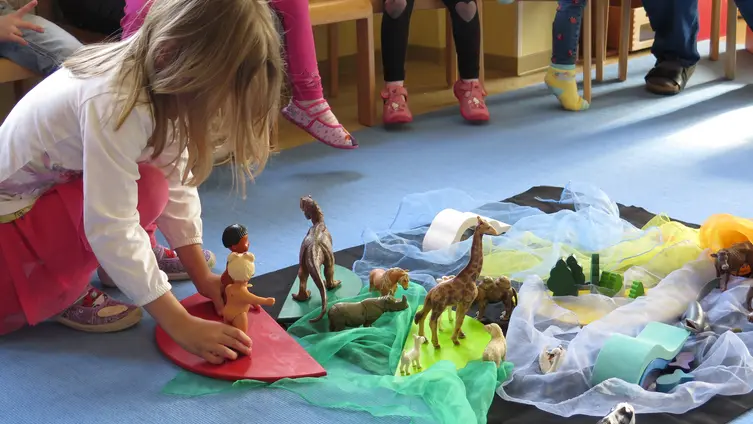 Kind spielt mit einer Figur am Boden, andere Kinder schauen zu 