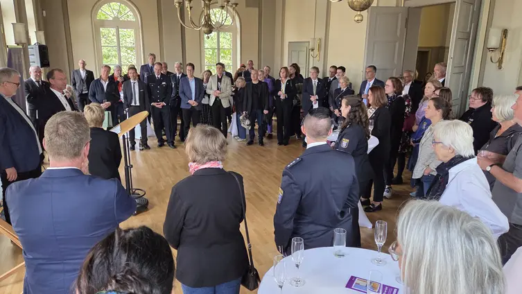 Eine große Anzahl von Personen stehen in dem prächtigen Saal im Kreis, manche tragen eine Polizeiuniform.