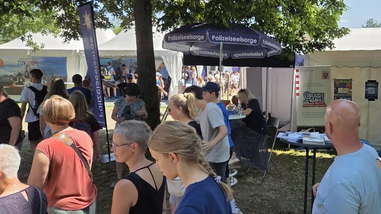 Viele Menschen sind unterwegs. Im Hintergrund ist ein Sonnenschirm der Polizeiseelsorge zu sehen.