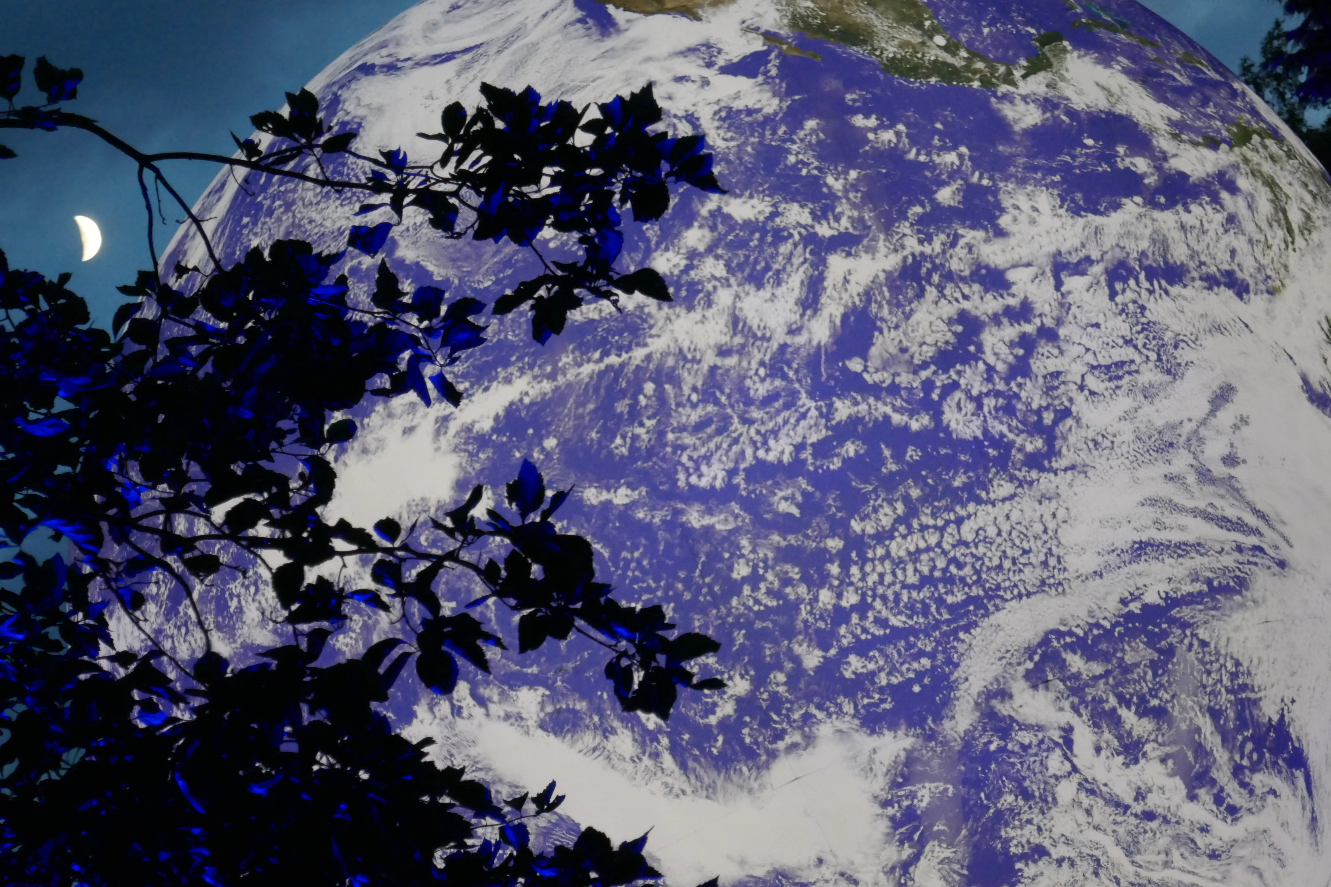 Die Weltkugel "Gaia" des Künstlers Luke Jerram leuchtet, im Hintergrund sieht man eine Mondsichel.