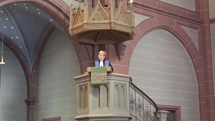 Die Pfarrerin steht oben auf der Kanzel, viel Gemäuer umgibt die Kanzel.