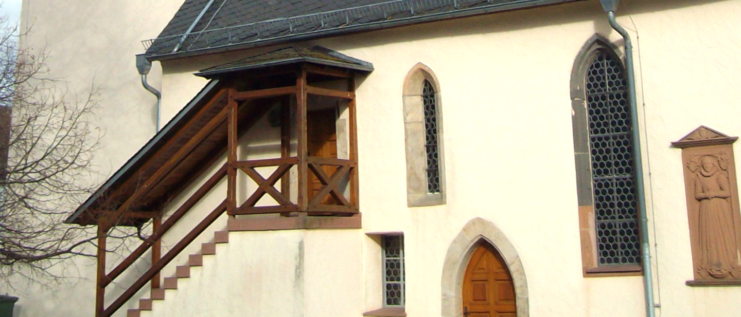 Weiße Kirchenmauer mit Fenstern und Treppe mit Holzgeländer und Überdachung